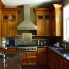 a kitchen with wooden cabinets and granite counter tops, an oven hood over the stove