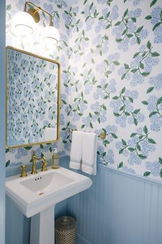 a bathroom with blue and white wallpaper, gold faucet, sink and mirror