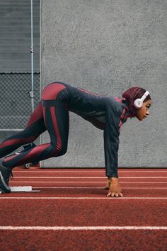 a woman in black and red running on a track with headphones around her ears