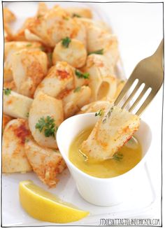 a fork with some food on it next to a bowl of soup and lemon wedges