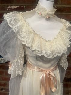 a white dress with lace and bows on the neckline is displayed in front of a brick wall