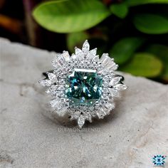 a fancy blue diamond ring sitting on top of a white stone slab with green leaves in the background