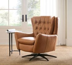 a brown leather chair sitting in front of a window next to a table with a book on it