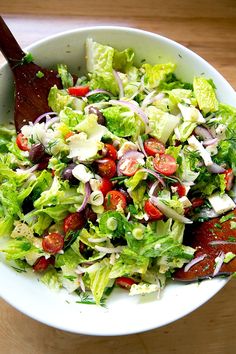 a salad with lettuce and tomatoes in a white bowl on a wooden table