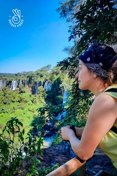 a woman standing on top of a wooden railing next to a lush green forest covered hillside