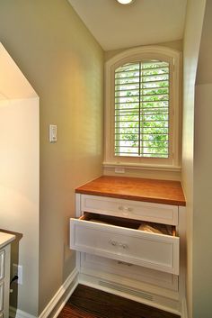 an empty room with white drawers and a wooden counter top in the corner next to a window