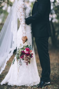 a bride and groom standing in the woods holding each other's wedding bouquets