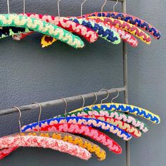 several colorful hair clips hanging on a clothes rack next to a gray wall with blue, green, red, yellow and white designs