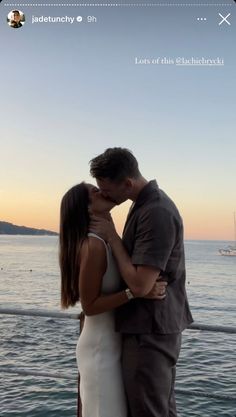 a man and woman kissing in front of the ocean