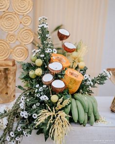 an arrangement of fruit and flowers on a table with other items in the back ground