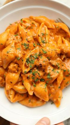 a white bowl filled with pasta covered in sauce and parsley on top of it