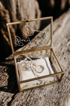 an open box with two wedding rings in it sitting on a piece of drift wood