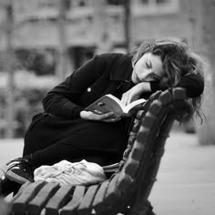 a woman is sitting on a bench reading a book while holding her head in her hands