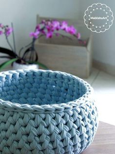 a blue woven bowl sitting on top of a wooden table next to purple flowers in a vase