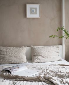 an unmade bed with white linens and a plant on the nightstand next to it