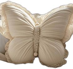 a white butterfly shaped pillow with lace on the back and wings, sitting in front of a