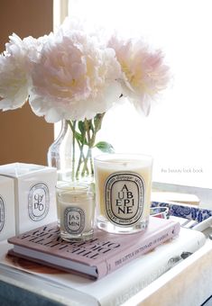 two candles are sitting on a table next to some books and flowers in a vase