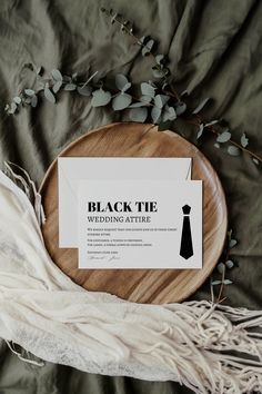 a wooden plate with a black tie card on it next to a white scarf and green leaves