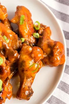 a white plate topped with chicken wings covered in sauce and green onion garnish