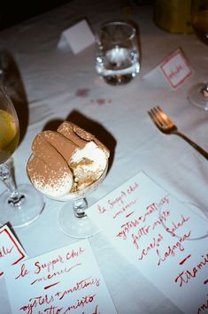 a table topped with wine glasses filled with desserts and writing on paper next to each other