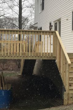 a wooden staircase leading up to a house with snow falling on the ground and trees in the background