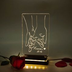 a couple holding hands in the shape of a glass block with lights on it and a rose next to it