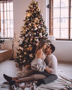 a man and woman sitting in front of a christmas tree