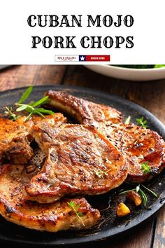 a black plate topped with pork chops on top of a wooden table