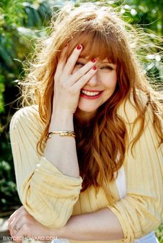 a woman with red hair smiling and holding her hand to her face