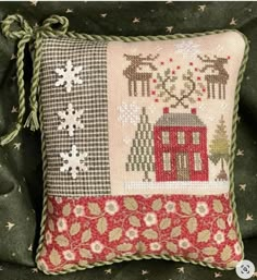 a cross stitch pillow with a house and deers on the front, surrounded by snowflakes