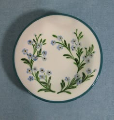 a white plate with blue and green flowers painted on the side, sitting on a blue table cloth