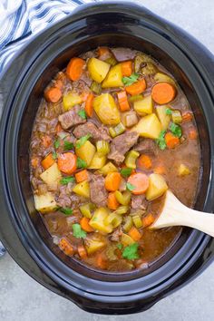 a crock pot filled with beef stew and carrots next to a blue towel