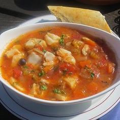 a white bowl filled with soup next to a piece of bread on top of a blue napkin