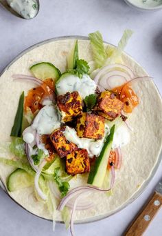 a taco filled with meat and vegetables on top of a white plate next to a knife