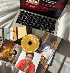 an open laptop computer sitting on top of a bed next to pictures and a dvd