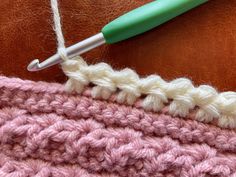 the crochet stitch is being worked on with a green handled crochet hook