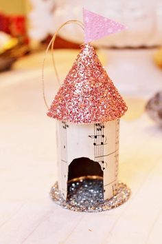 a small white birdhouse with pink and silver glitter on it's roof, sitting on a table