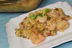 a white plate topped with rice and shrimp next to a casserole dish on a blue table cloth