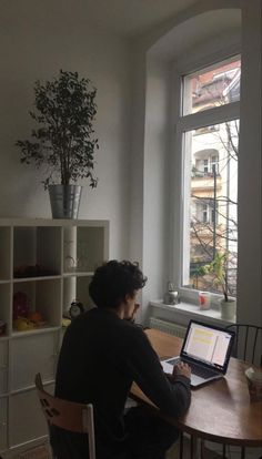 a man sitting at a table with a laptop computer in front of him and looking out the window