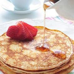 pancakes on a plate with syrup being drizzled over them and strawberries