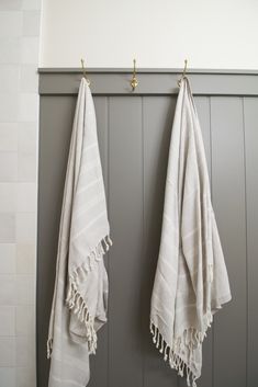 two white towels hanging from hooks in a bathroom