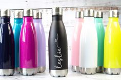 six different colored stainless steel water bottles lined up on a white wooden background with the word love written in cursive writing