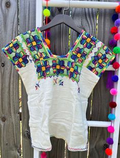 a white top with colorful pom poms hanging on a wooden fence