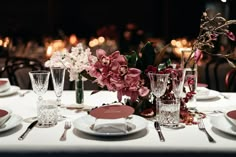 the table is set with plates, silverware and pink orchids in vases