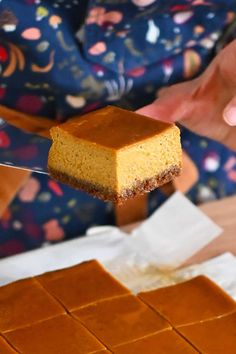 a person holding a piece of cake on top of a wooden cutting board with a knife