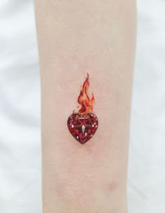 a heart shaped tattoo on the ankle with fire coming out of it's center