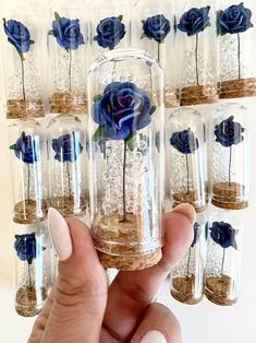 a hand holding a glass jar filled with blue roses and sand in each one's hands