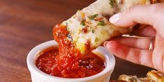 a person dipping sauce onto a piece of pizza in a small white cup on top of a wooden table