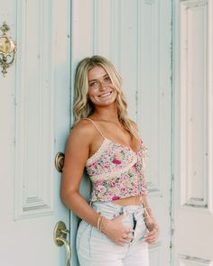 a woman standing in front of a blue door wearing white jeans and a floral crop top