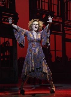 a woman in a dress on stage with her arms outstretched